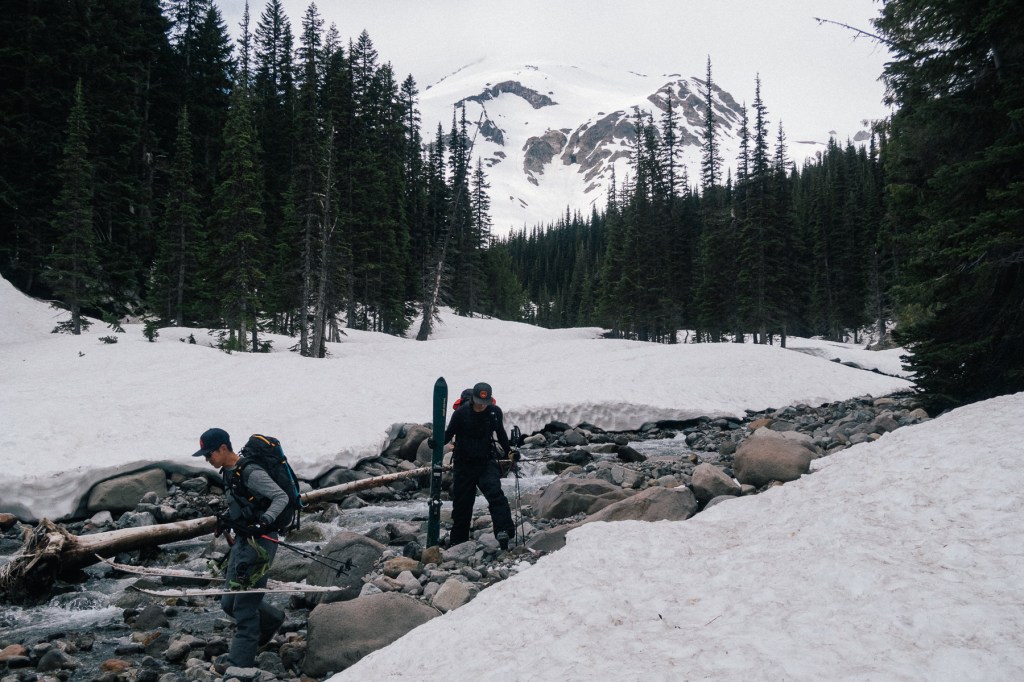 Backcountry tourers crossing a creek at the snowline in Glacier Basin Mount Rainier