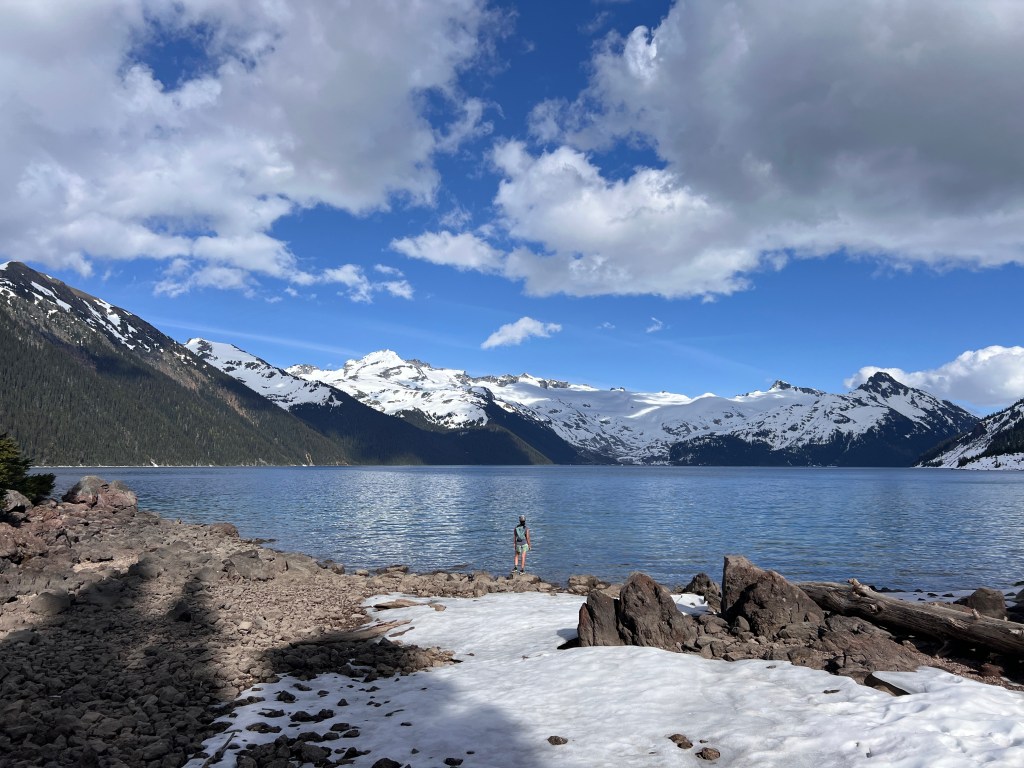 Panoramic scenic view of Garibaldi Lake surrounded by snow covered mountains during spring shoulder season